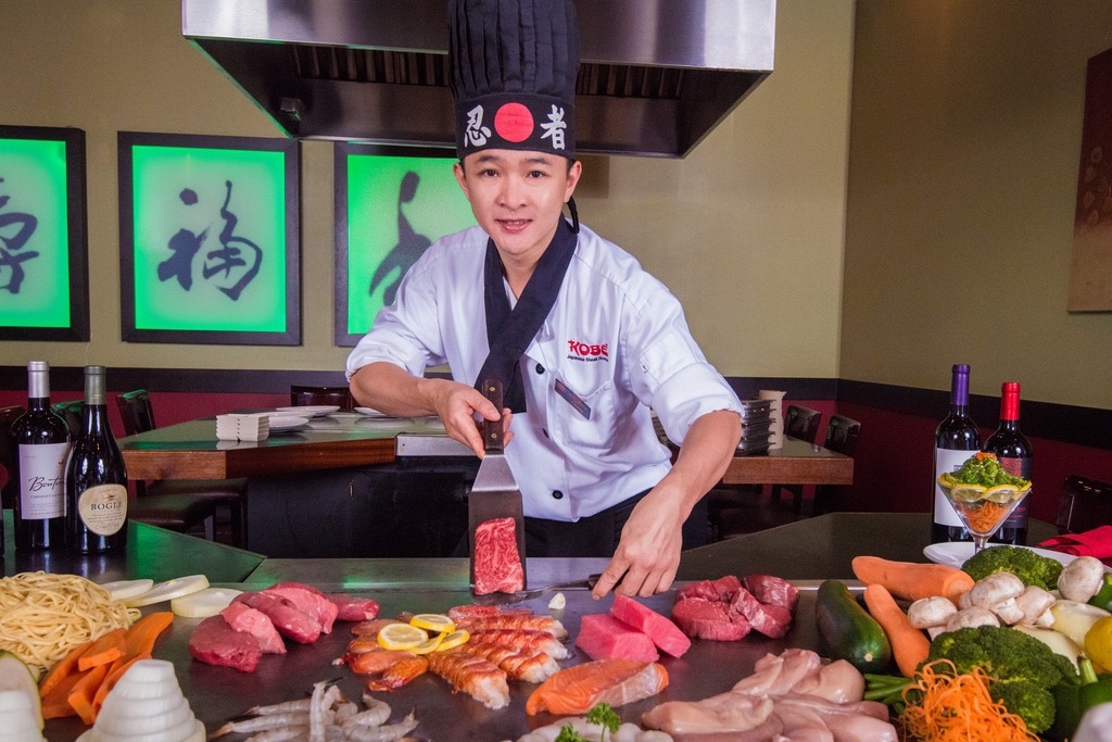 Teppanyaki chef with Wagyu Beef and other foods on grill.