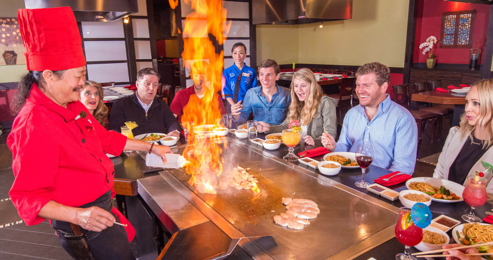 Group of people watching a Kobe chef set food on fire