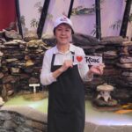 Kobe employee wearing I Love Kobe hat and holding I Love Kobe sign