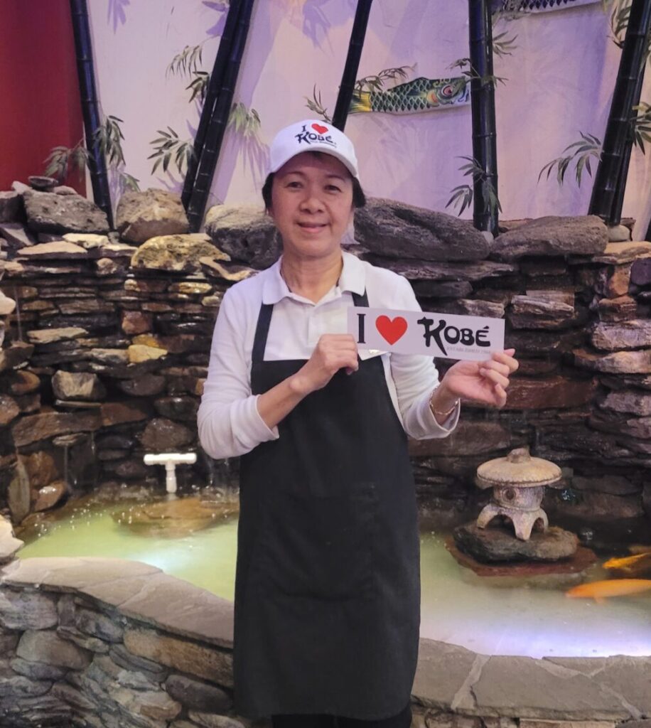 Kobe employee wearing I Love Kobe hat and holding I Love Kobe sign